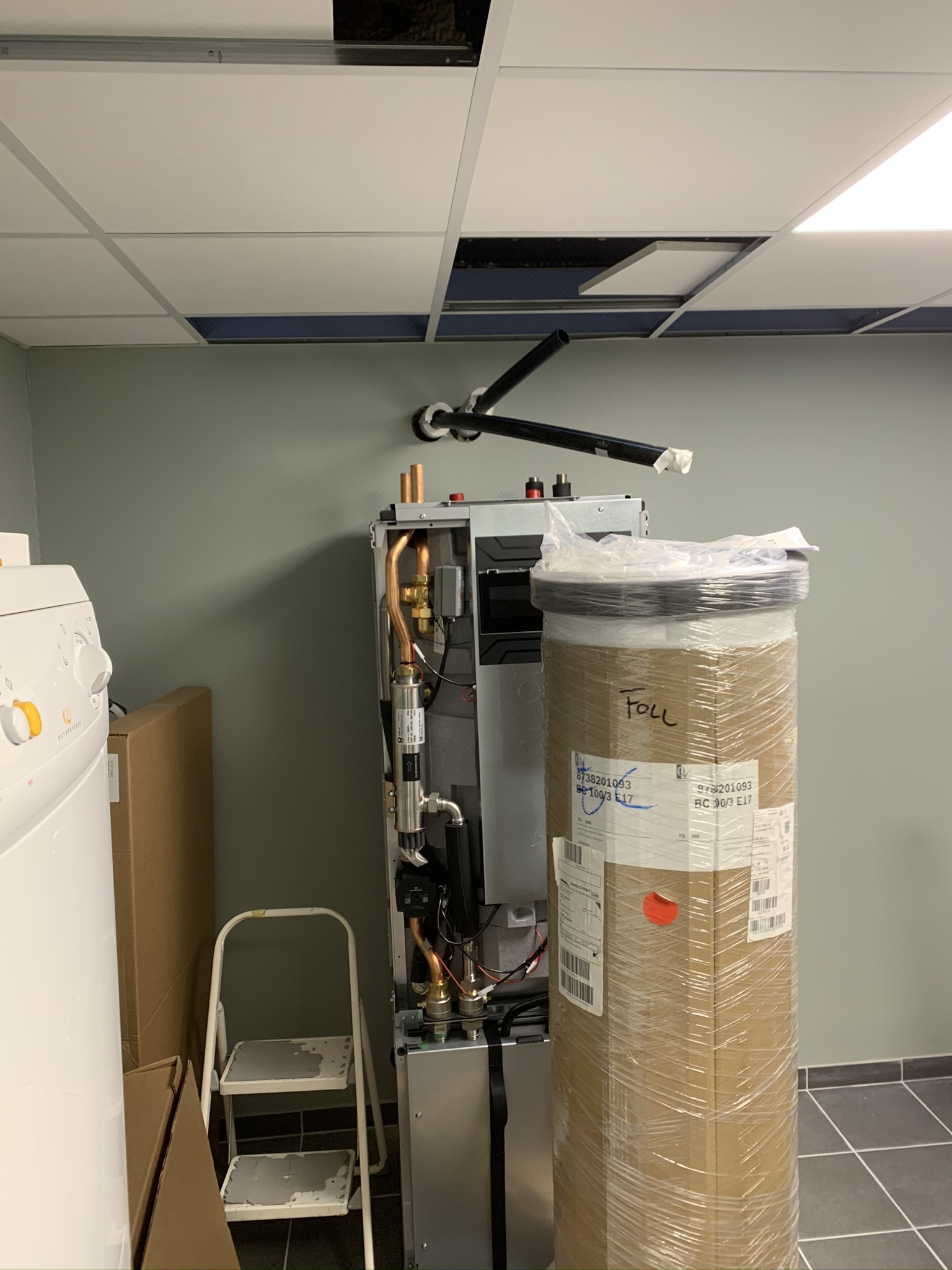 Varmepumpen under montering, med tank og rør gjennom taket