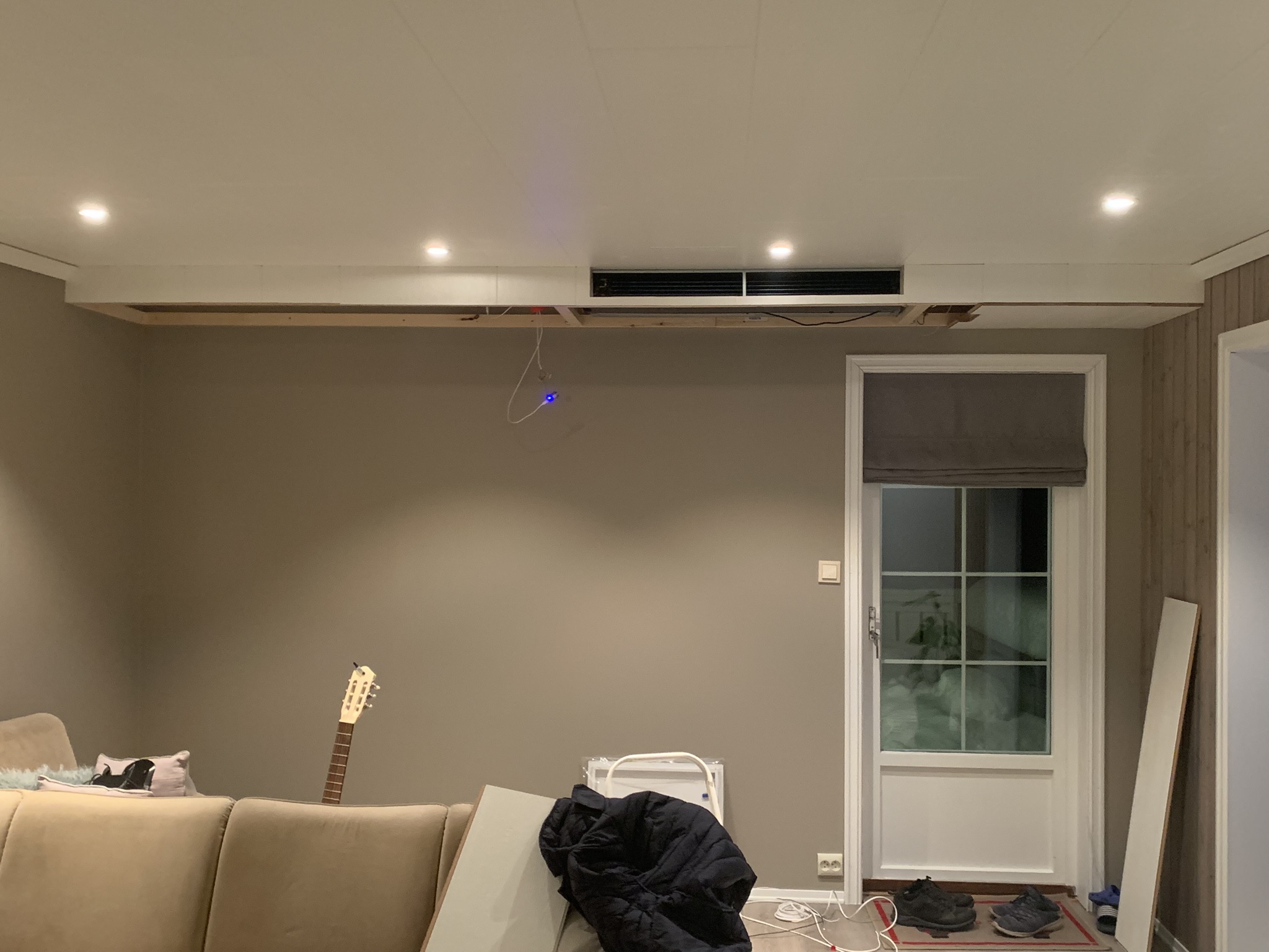 Stue med viftekonvektor nesten ferdig — sofa og gitar synlig, én ledning henger igjen.